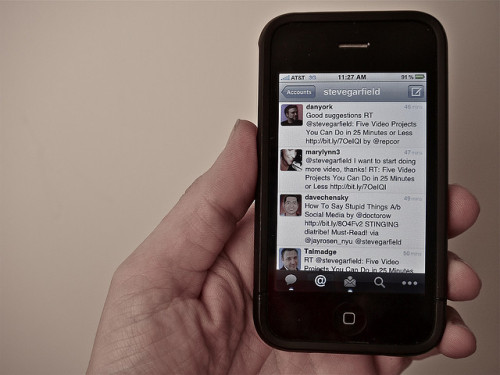 closeup of an iPhone displaying Twitter client, held by a white, male hand.
