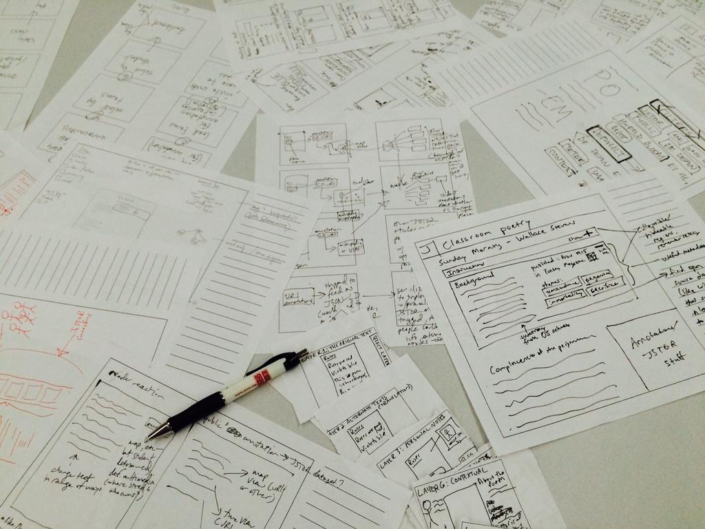 Sheets of paper with hand-drawn sketches of a web annotation interface, lying on a table.