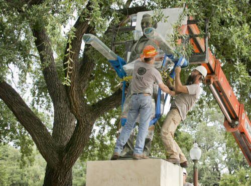 Image shows two men positioning a crane to remove the plastic-wrapped statue of Jefferson Davis.