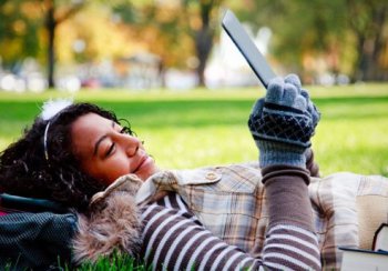 A young woman reads an iPad on the grass.