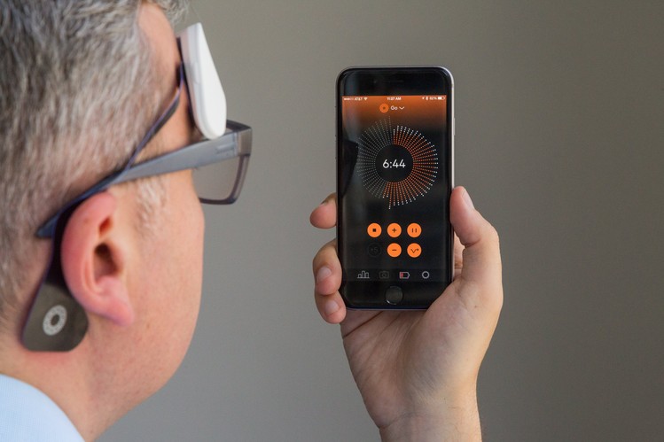 Image of a man wearing the Thync device and looking at a phone displaying the Thync interface