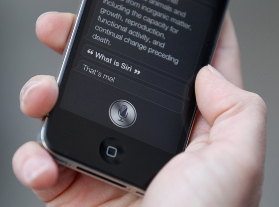 Close up Photograph of a black apple iPhone, engaging with the Siri function. The photo shows a conversation where the user asked, "what is Siri?" and Siri responded "that's me!"