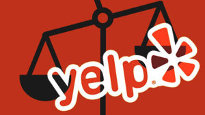 This is a picture of the Yelp logo with a symbolic scale in the background indicating the lawsuits against Yelp. The picture is mostly in red, the scale in the background is in black. The letters and the Yelp logo are mostly in white.