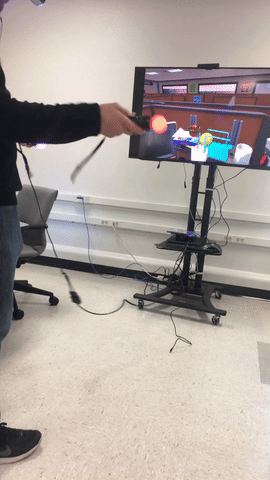 GIF of a D.W.R.L. Staffer using the playstation controller to pick up a virtual ball. The staffer has the virtual reality headset on, and their hands are being tracked by two remotes, one in each hand.