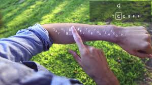 An image of a holographic keyboard on a person's left forearm, he or she is pressing a key on it with his or her right pointer finger.