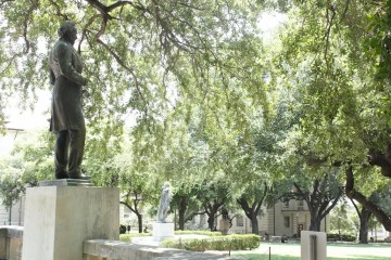 Image shows two statues on the UT South Mall, Jefferson Davis to the left and another on the right, with a background of trees.