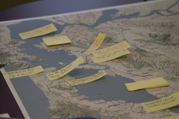 A close-up of a topographical map with a number of yellow sticky notes attached to it. The notes have different people's handwriting on them.