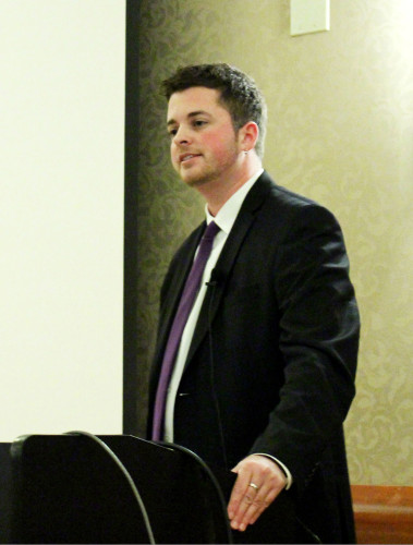 Dr KJ Rawson standing behind a podium in front of a blank screen