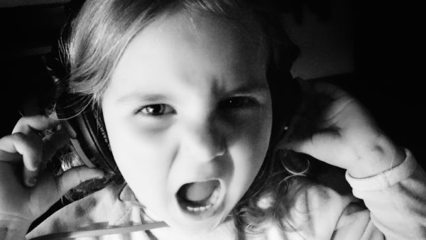 Black and white picture of a little girl wearing big headphones, looking like she's screaming.