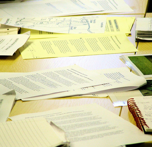 Wooden desk strewn with loose papers and spiral notebooks